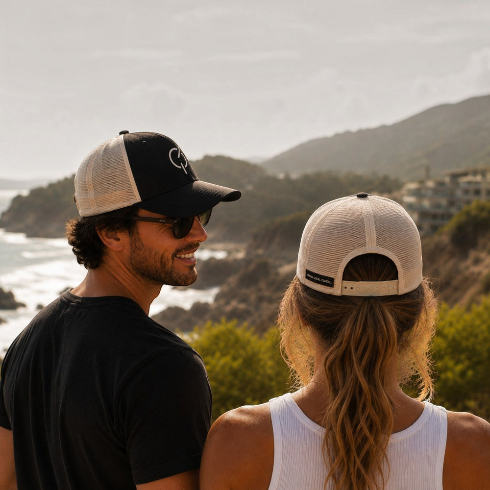 area 609 Core Trucker Hat in black and ecru mesh worn by a man and woman overlooking a coastal landscape