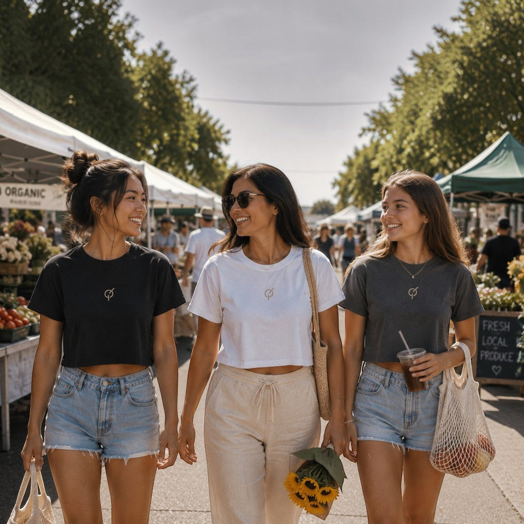 Three women wearing area 609 cotton cropped t-shirts in black, white, and coal at a sunny outdoor farmers market.